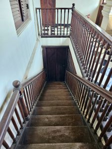 A steep, polished wooden staircase with classic railings inside the Hill Palace, Thrippunithura, Kerala, showcasing colonial architecture. 