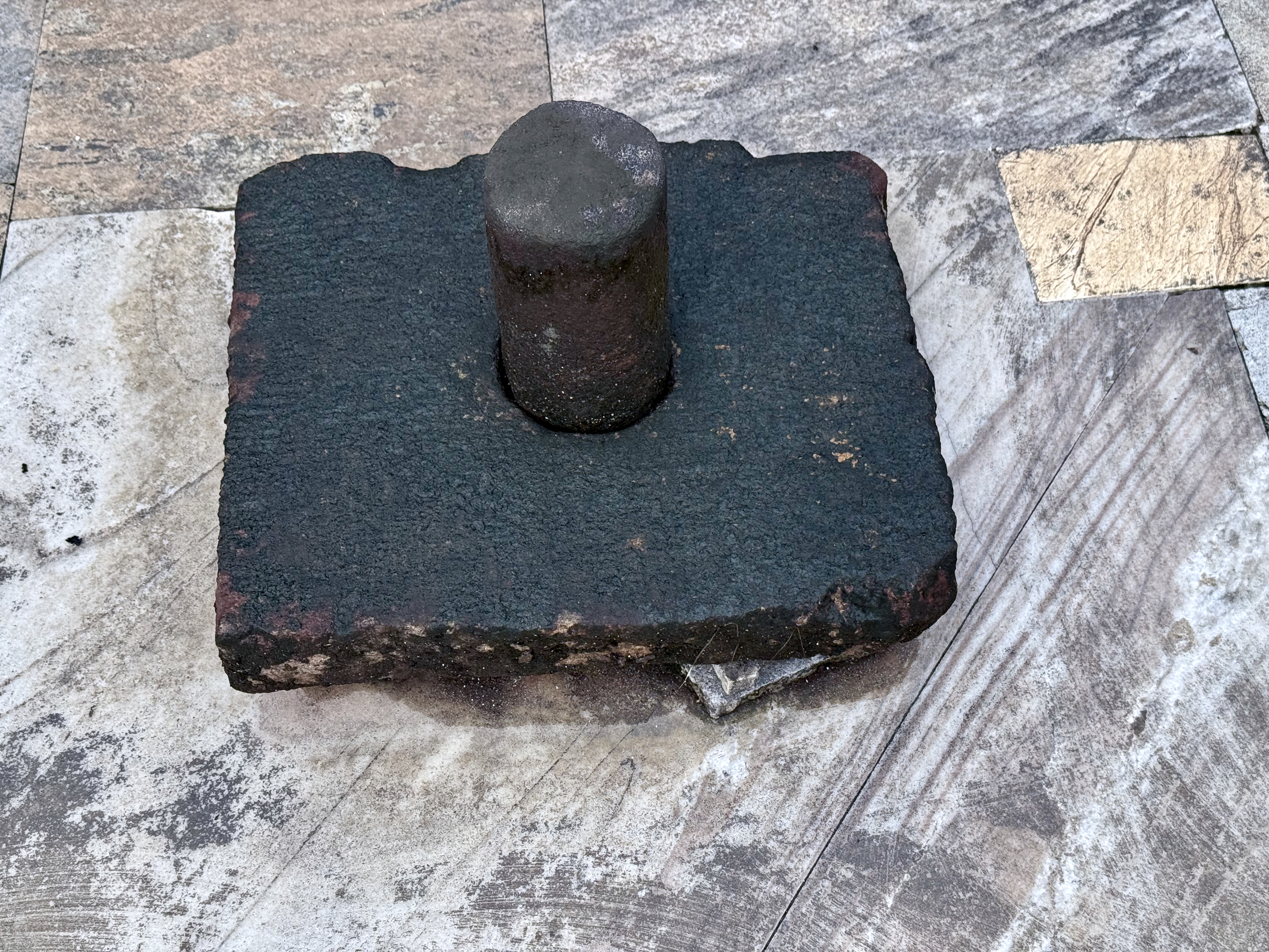 An ancient-looking Shiva Linga made of dark stone, placed on a temple floor made of natural stone tiles, was captured from Sree Shiva Vishnu Temple, Perumanna.