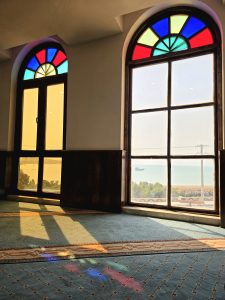 A spacious room with two arched stained-glass windows, casting colorful reflections on a patterned blue carpet.