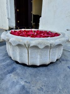 A white marble bowl filled with red rose petals is placed on the stone floor at Monsoon Palace, Sajjangarh, Udaipur. This bowl is used as a simple floral decoration near the palace entrance.