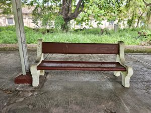 A cement bench, painted in brown and cream, sits under a canopy on the old railway platform at Cochin Harbour Terminus, offering a peaceful and nostalgic view from Kochi. 