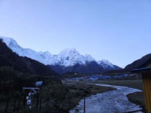 A dawn view of snow-capped mountains with a calm stream in grassy fields.