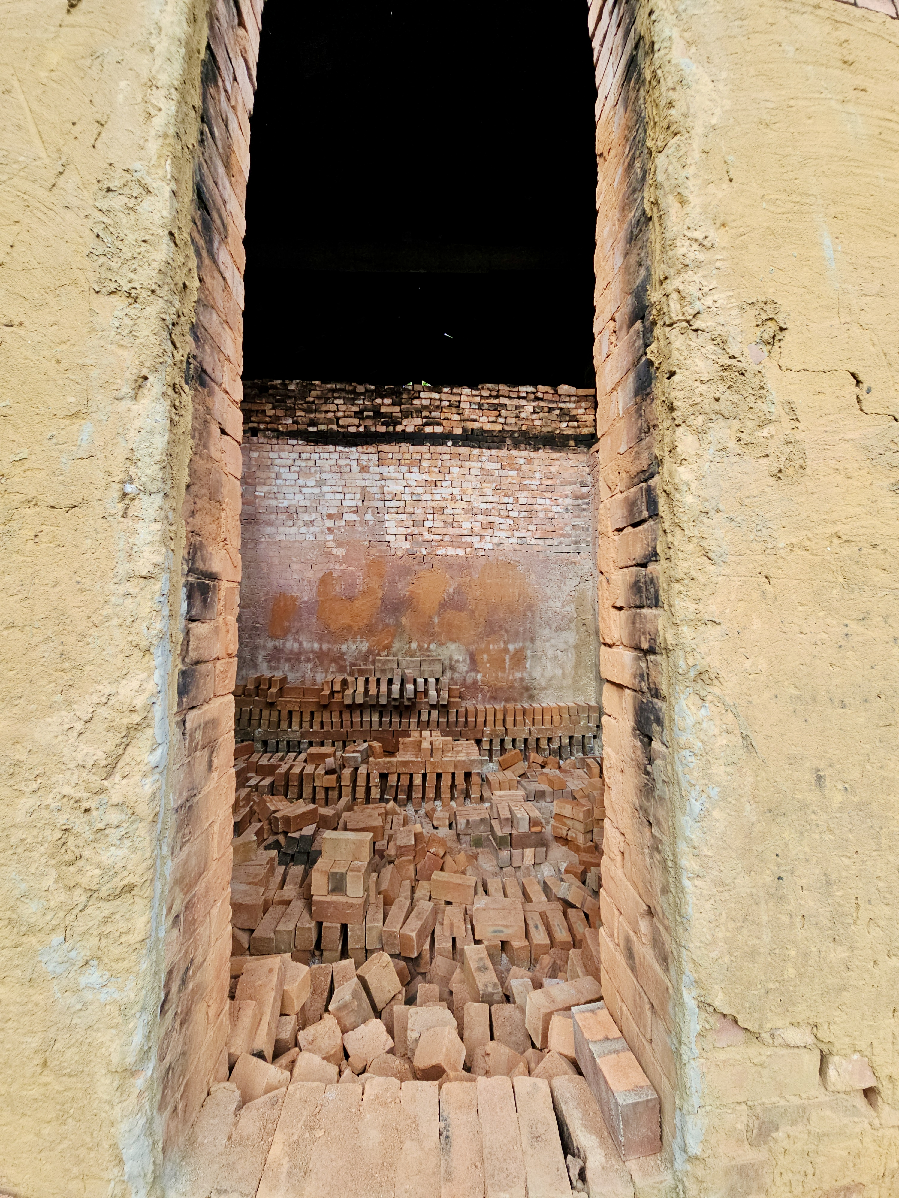 A framed view through the kiln entrance showing brick stacks ready for firing. Taken at a local brick kiln in Perumanna, Kozhikode, Kerala. 