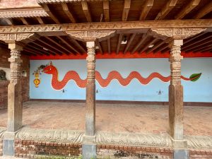 A bright red snake mural on a temple wall, bordered by wooden carved pillars and tiled flooring, was captured at Patan Durbar Square, Lalitpur, Nepal. 