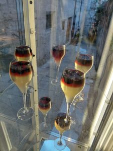 

Layered desserts with berries sit on glass shelves by a window overlooking a stone alley.
