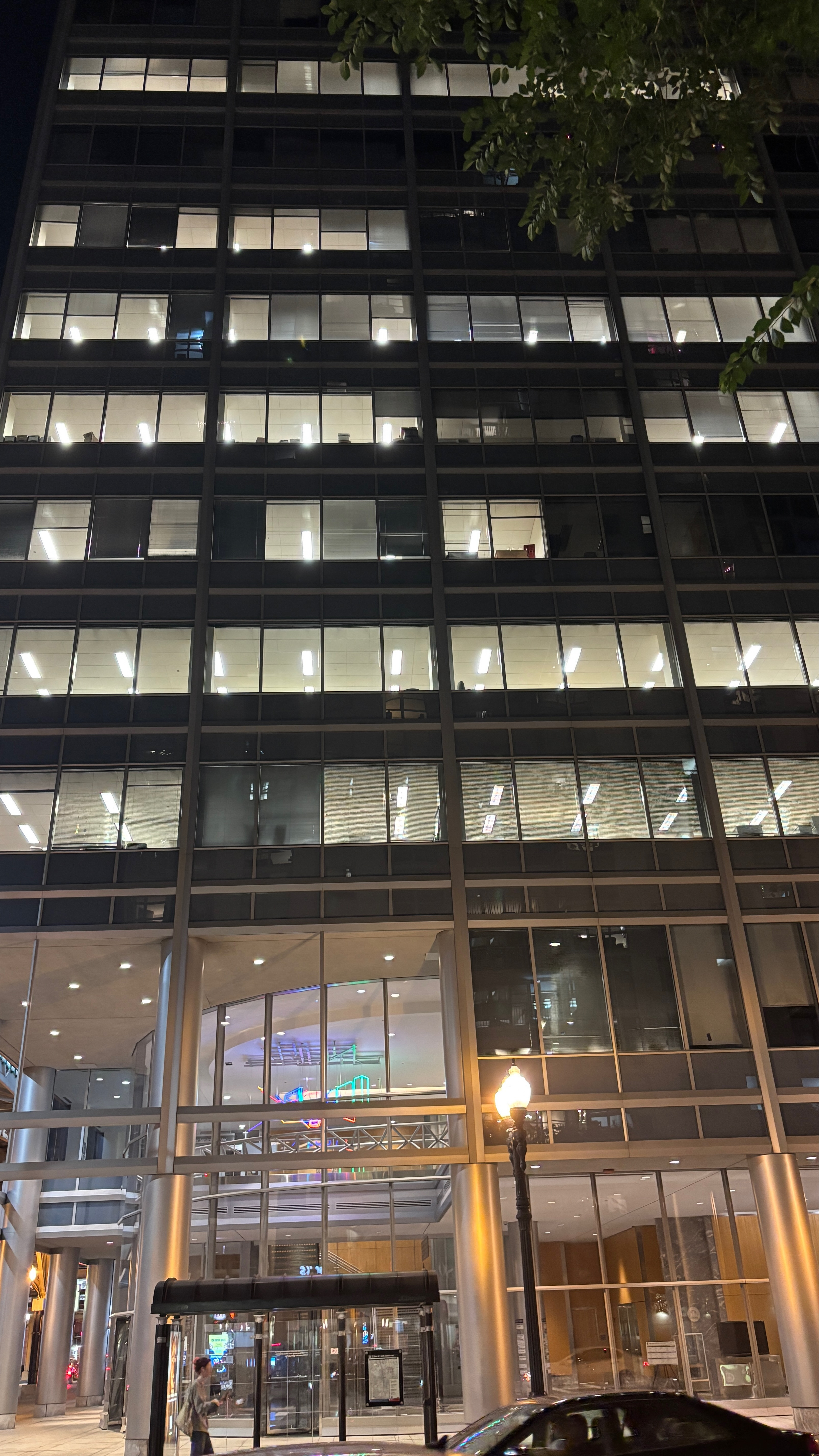 A tall building in a city at night, seen from across the street. All the windows are lit up.  The bottom two floors are an all-glass lobby.