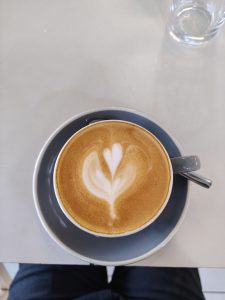 A close-up view of a cup of coffee with a heart-shaped latte art design on top, sitting on a gray saucer