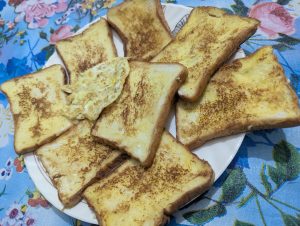 Golden brown homemade French toast slices stacked on a white plate, topped with a piece of cooked egg.
