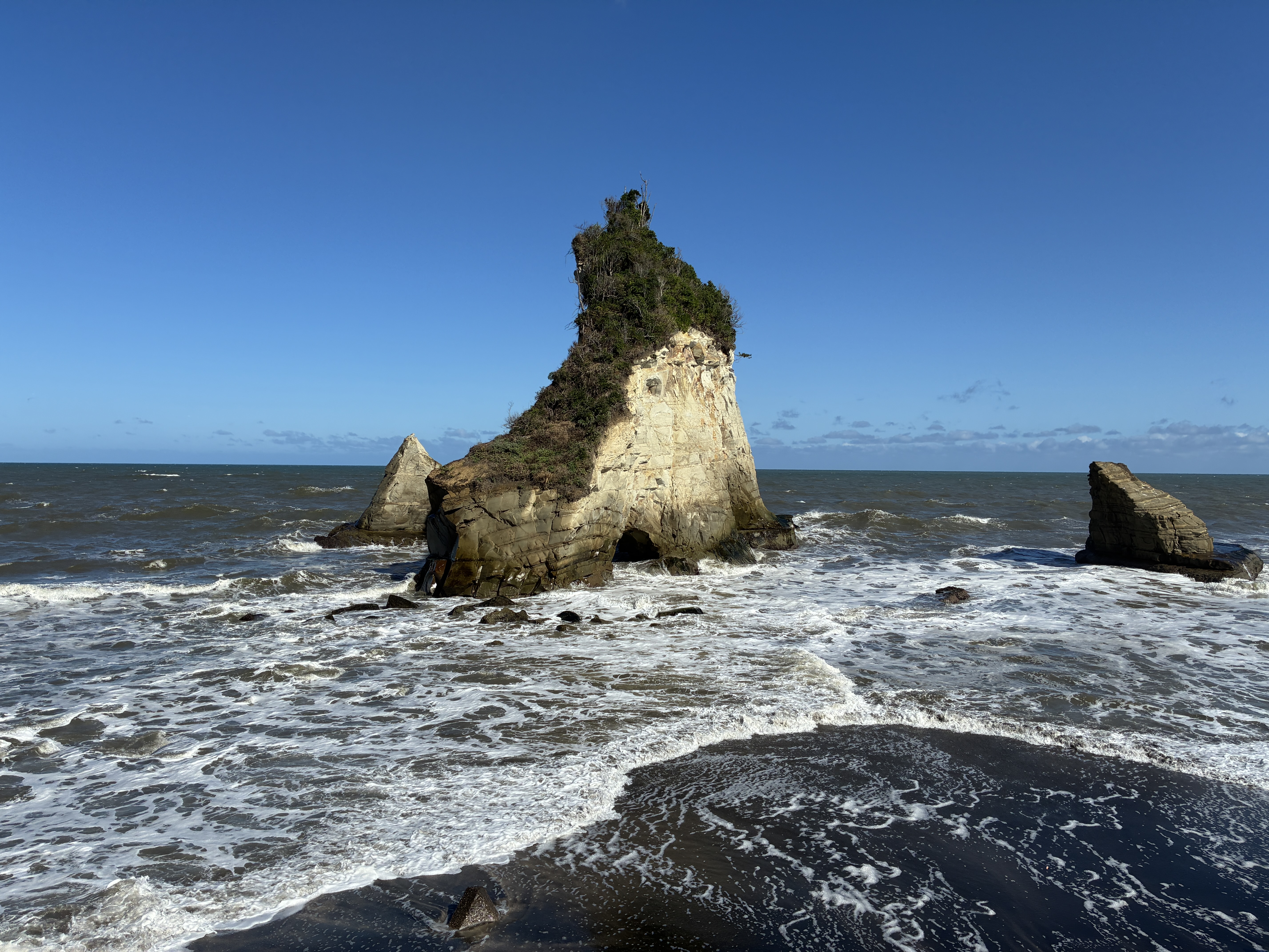 A scenic beach view featuring a prominent rock formation rising from the ocean.