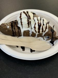 A tempting chocolate dessert served with two scoops of vanilla ice cream and chocolate syrup. Captured on a paper plate with wooden cutlery in Kozhikode, Kerala. 