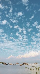 A serene coastal scene featuring a clear blue sky filled with fluffy white clouds. 