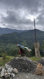 A person sits under a makeshift shelter made of tarps, positioned on a pile of gravel.