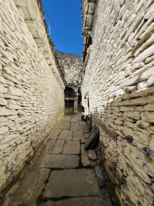 

A narrow Marpha  pathway flanked by white stone walls, leading towards a wooden door.