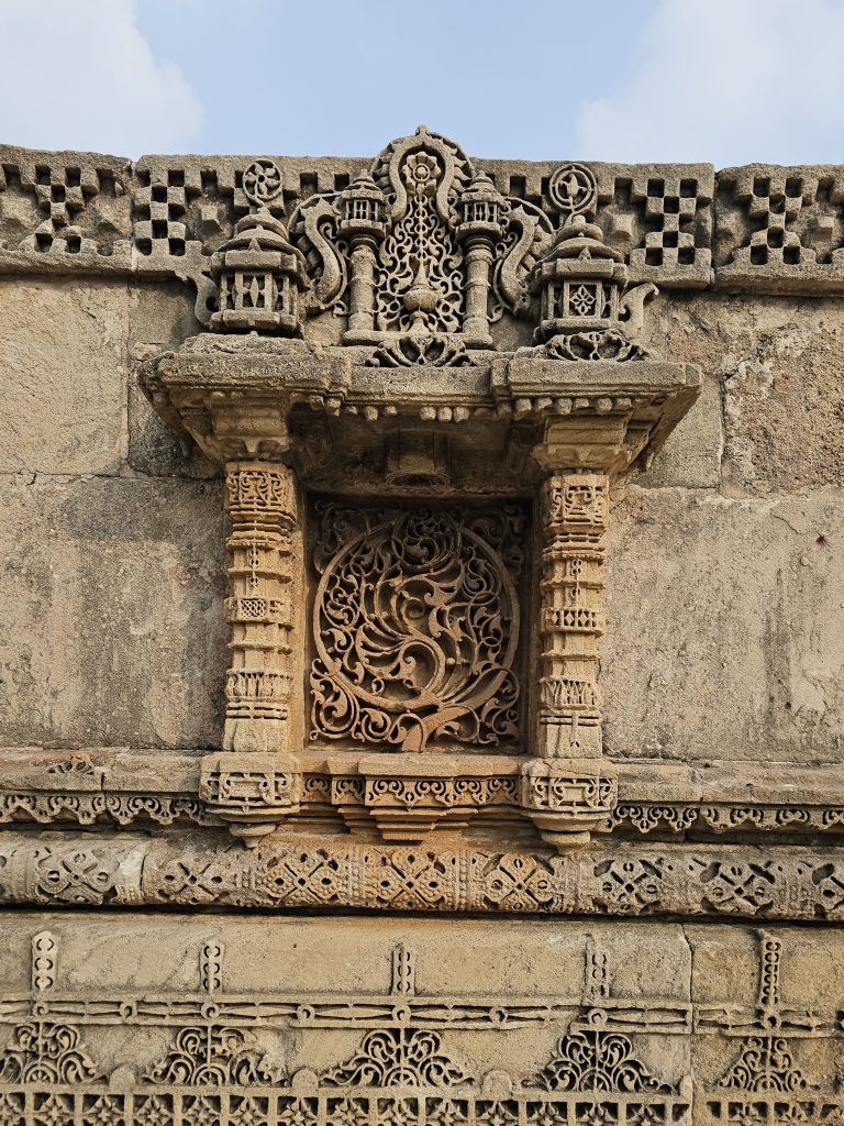 Circular floral jali (stone lattice) window framed by delicate sandstone carvings on the outer wall of Adalaj Stepwell (Gandhinagar, Gujarat).