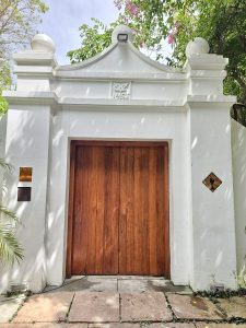 Elegant wooden gate framed by a white stucco archway with the number 1506 engraved and captured in Fort Kochi, Kochi, surrounded by tropical greenery and soft daylight. 