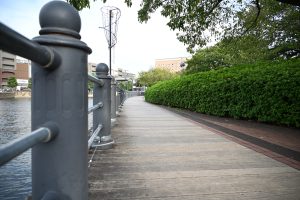 A scenic walkway along a river lined with metallic railing is visible.
