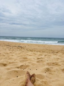 A close-up view of two feet resting in sandy beach ground, partially covered with sand.