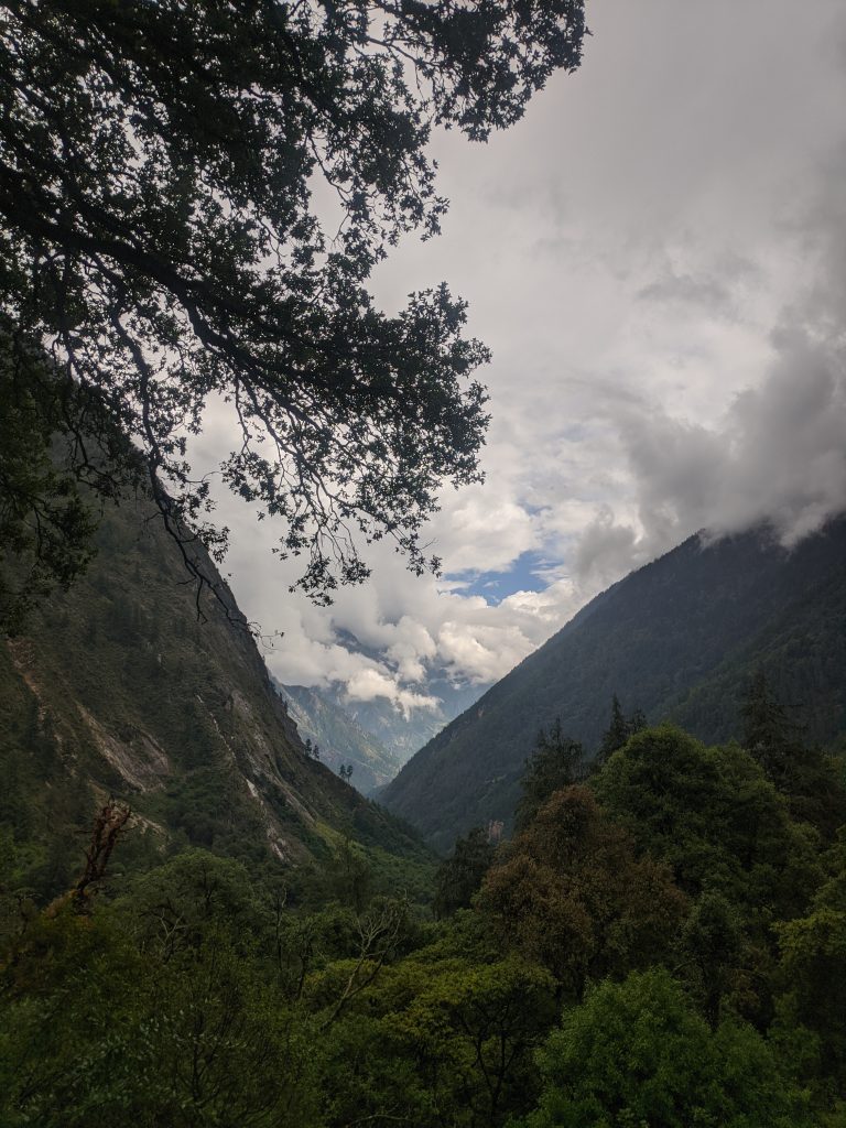 A serene mountain valley is framed by lush greenery and trees, with steep hillsides rising on either side.