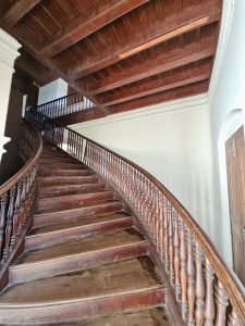 A sweeping wooden staircase with finely carved handrails and the ceiling featuring exposed beams inside the palace building. Shot at Hill Palace, Thrippunithura, Kerala. 