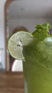 A close-up of a glass of green drink garnished with a slice of lime and fresh mint leaves.