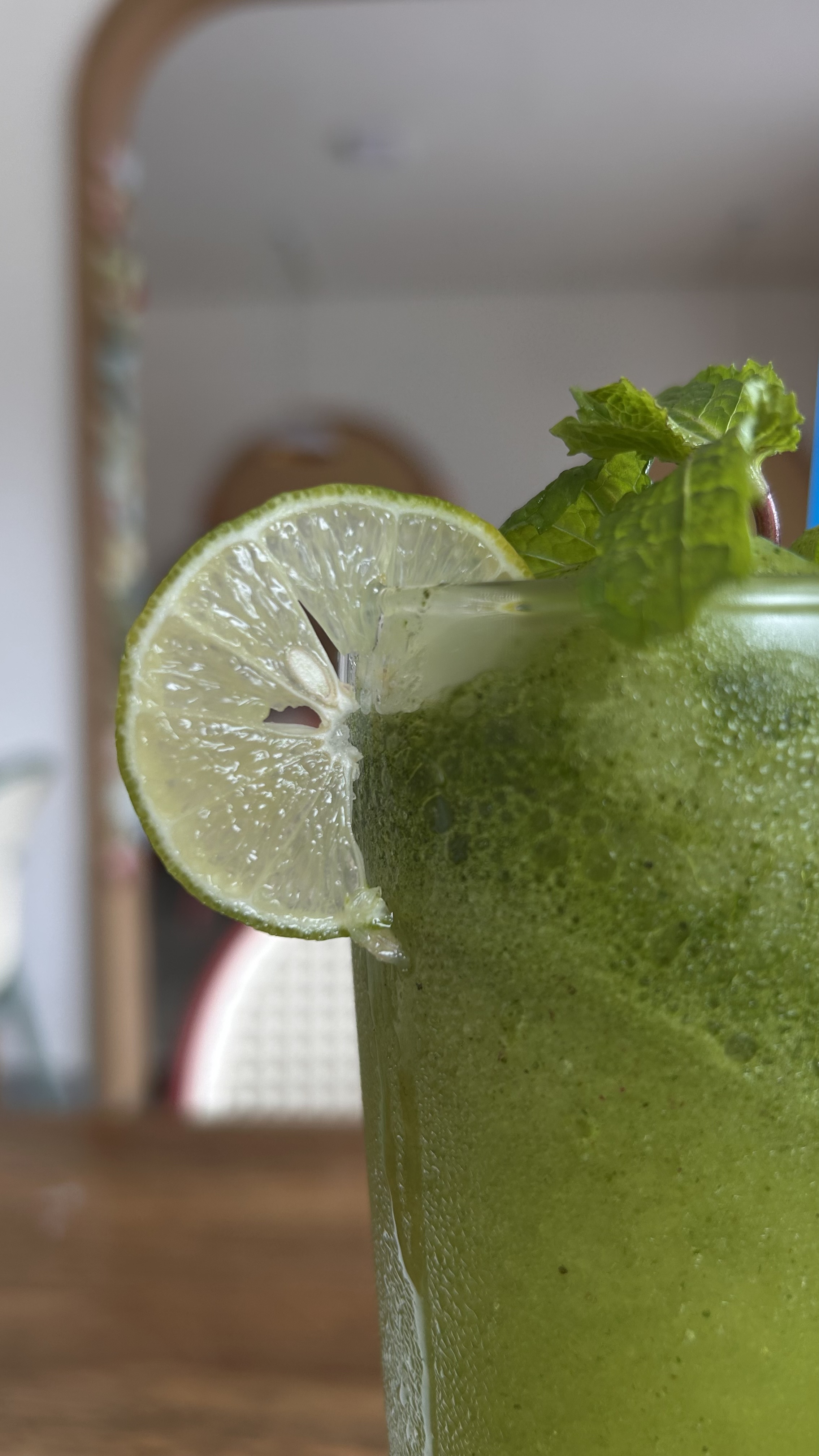 A close-up of a glass of green drink garnished with a slice of lime and fresh mint leaves.