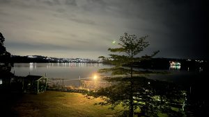 A nighttime view of a calm lake, with reflections of distant city lights shimmering on the water&#039;s surface.