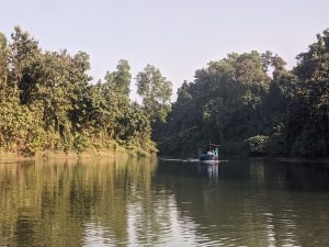 A peaceful scene on Foyez Lake in Chittagong, Bangladesh, as a boat gently glides through the calm waters. The surrounding lush greenery reflects perfectly on the water’s surface, capturing the serene beauty of this popular destination