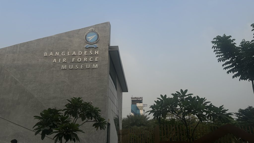 A picture of a Bangladesh Air Force Museum entrance gate with blue sky and trees.