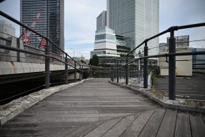 A wooden plank walkway with railings on both sides, leading to modern buildings in Kanagawa, Japan.