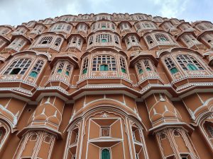 A close-up view of a historical building featuring intricate architectural details. The perspective is upwards, emphasizing the height and layering of the façade against a cloudy sky. Havamahal in Jaipur
