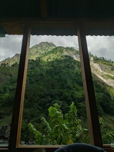 A view from the inside of a wooden structure overlooks a lush green mountainous landscape. 