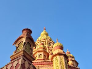 Side angle of detailed golden-yellow and red temple domes on Parvati Hill, Pune, under a clear blue sky.