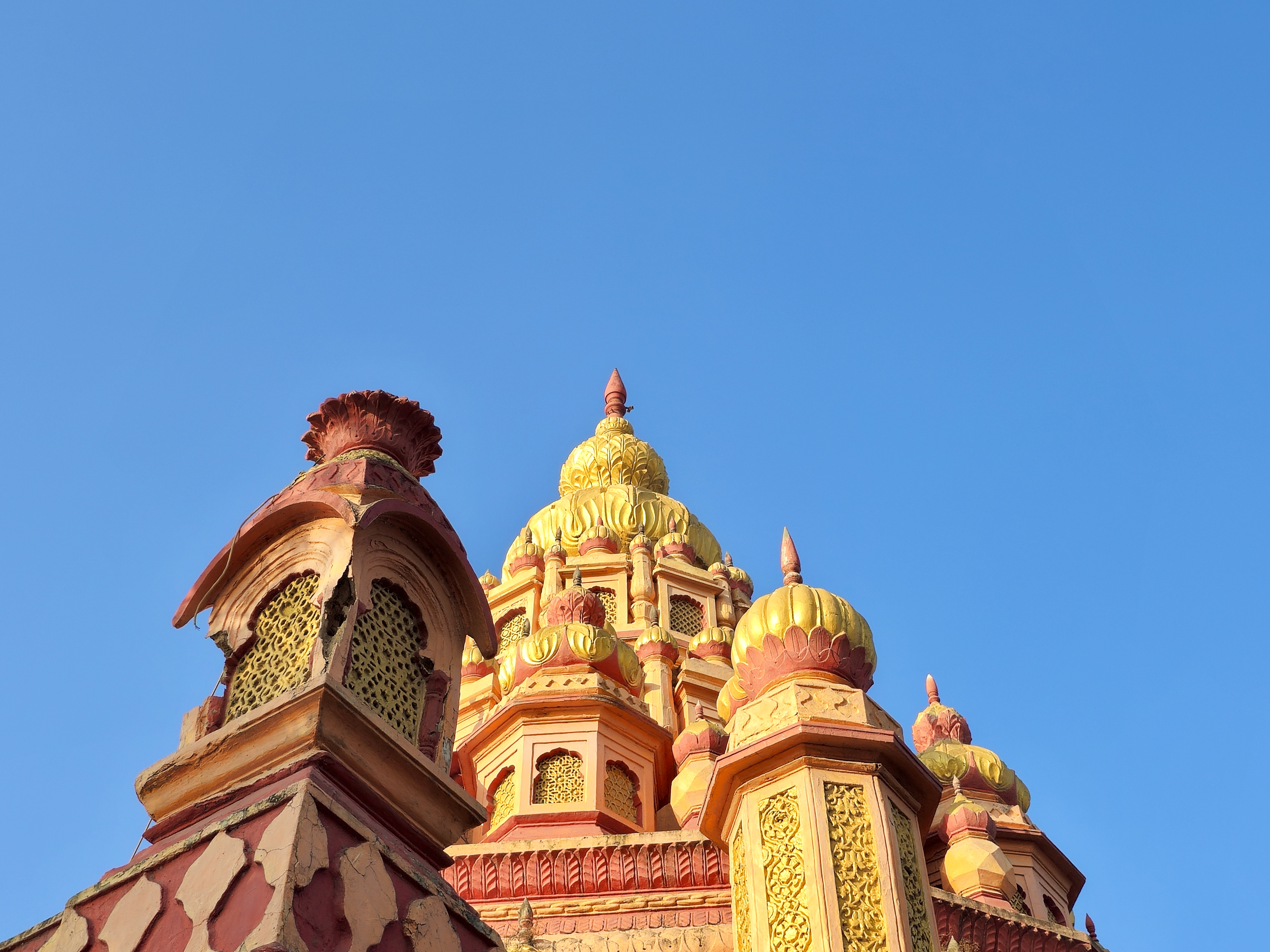 Side angle of detailed golden-yellow and red temple domes on Parvati Hill, Pune, under a clear blue sky.
