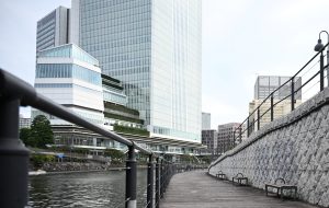 A modern waterfront in Kanagawa, Japan, with a wooden walkway along the river and a stone wall on one side