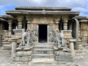 The entrance of the Bucesvara Temple in Koravangala, Hassan, Karnataka. The beautifully carved temple features two majestic elephant sculptures on either side of the steps and detailed stone carvings of Hindu deities on the pillars. The architecture shows the Hoysala style with intricate details preserved in stone. 
