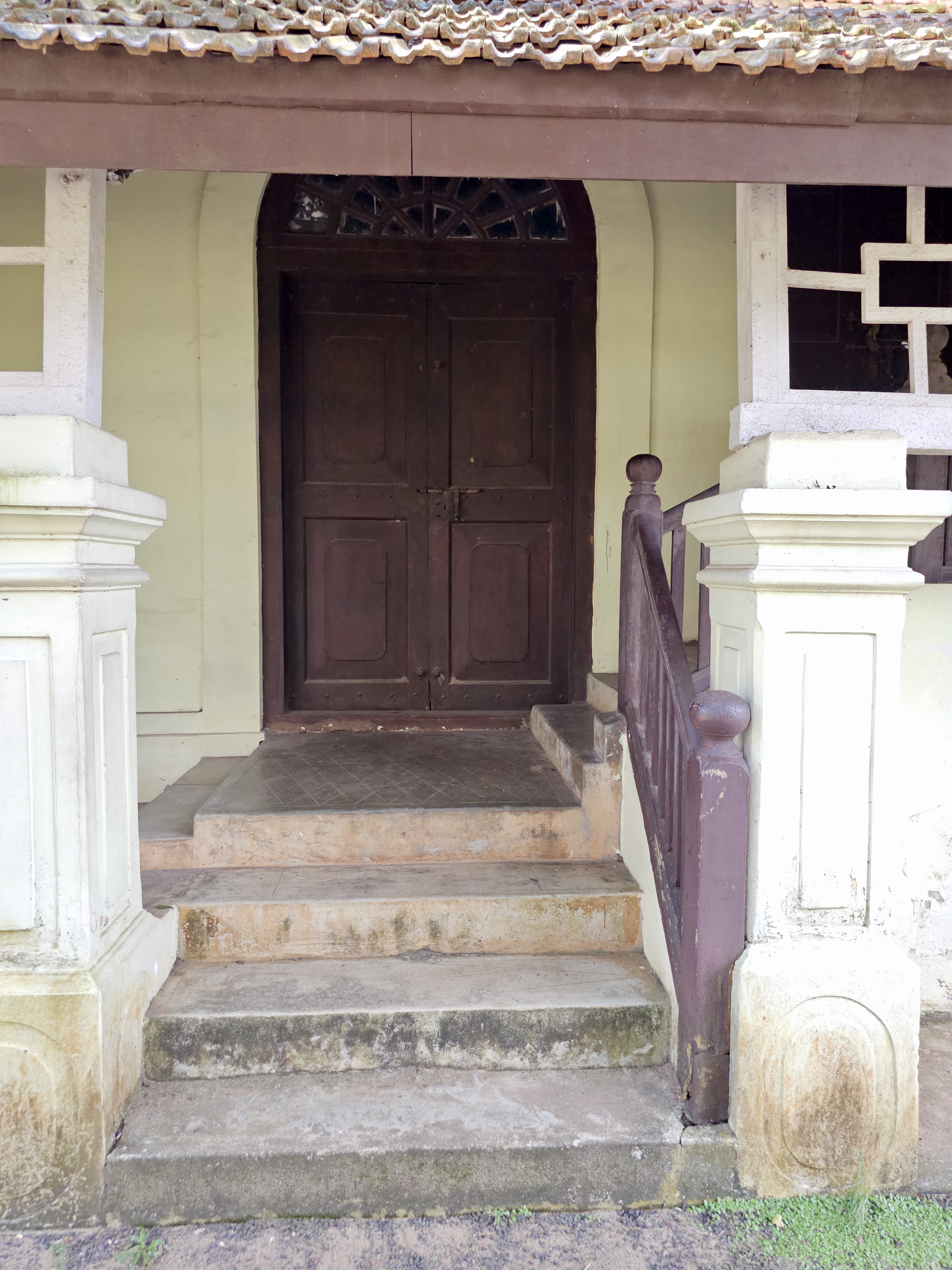 A close-up of the entrance steps and wooden double doors of an old heritage building at Hill Palace, Thrippunithura. 