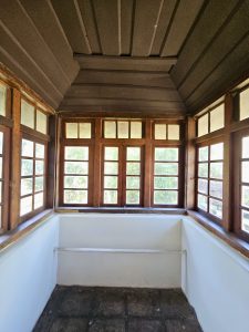 An enclosed corner balcony space surrounded by wooden-framed glass windows, located in the upper floor of Hill Palace, Thrippunithura, Kerala. 