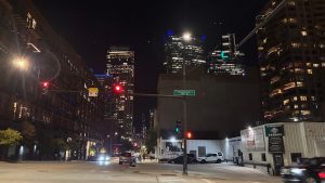 A night scene of an intersection in Chicago. In the center is a tall post with a light at the top, a street sign in the center, and an arm coming off it with a red stop light over the street.
