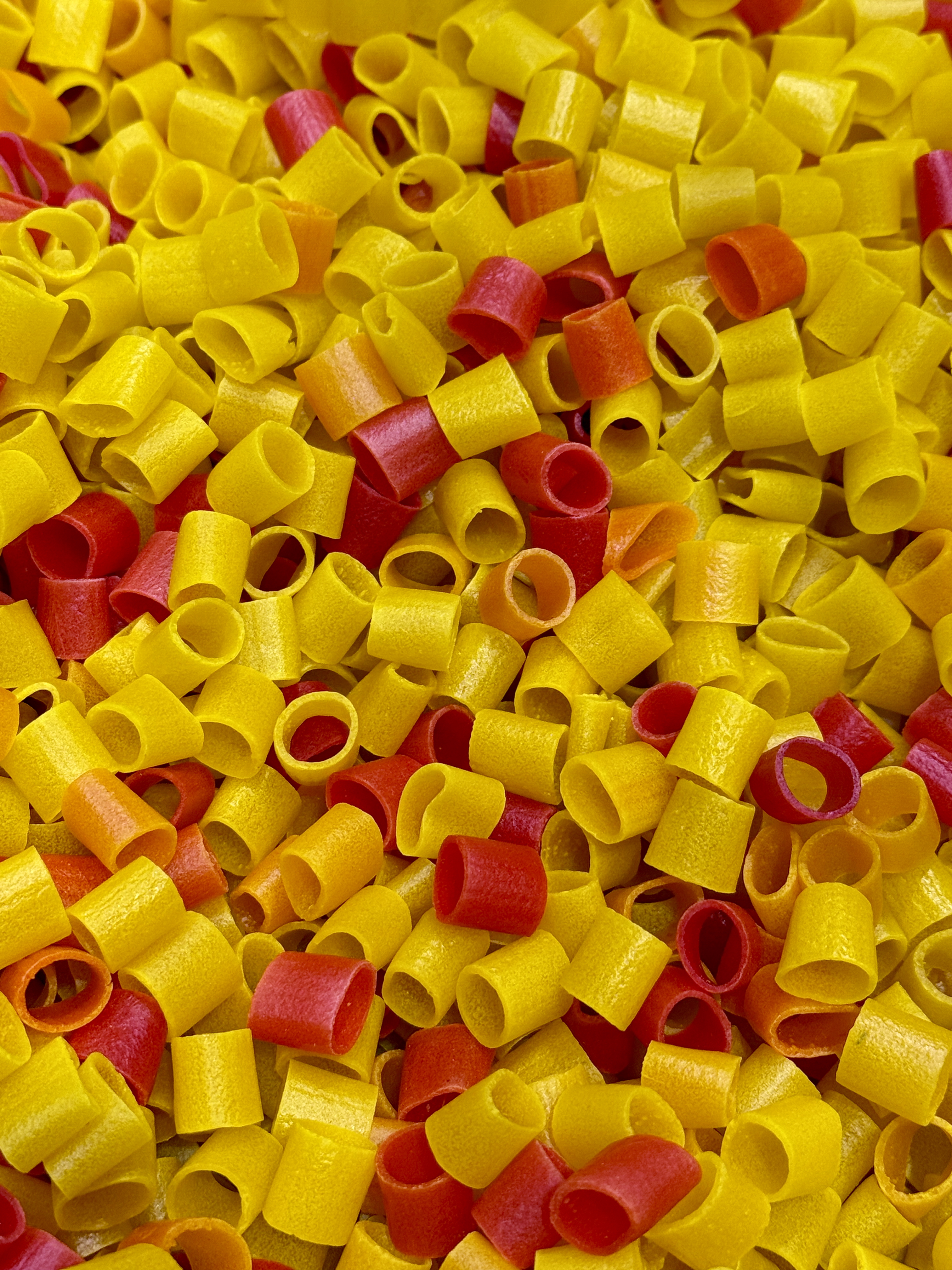 A close-up photo of colorful uncooked snack rings in bright yellow, red, and orange shades. This vibrant image of Kerala’s popular fryums was taken in Kozhikode, Kerala.