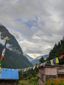 A mountainous landscape under overcast skies, featuring a traditional building with a pink exterior and a blue roof. 