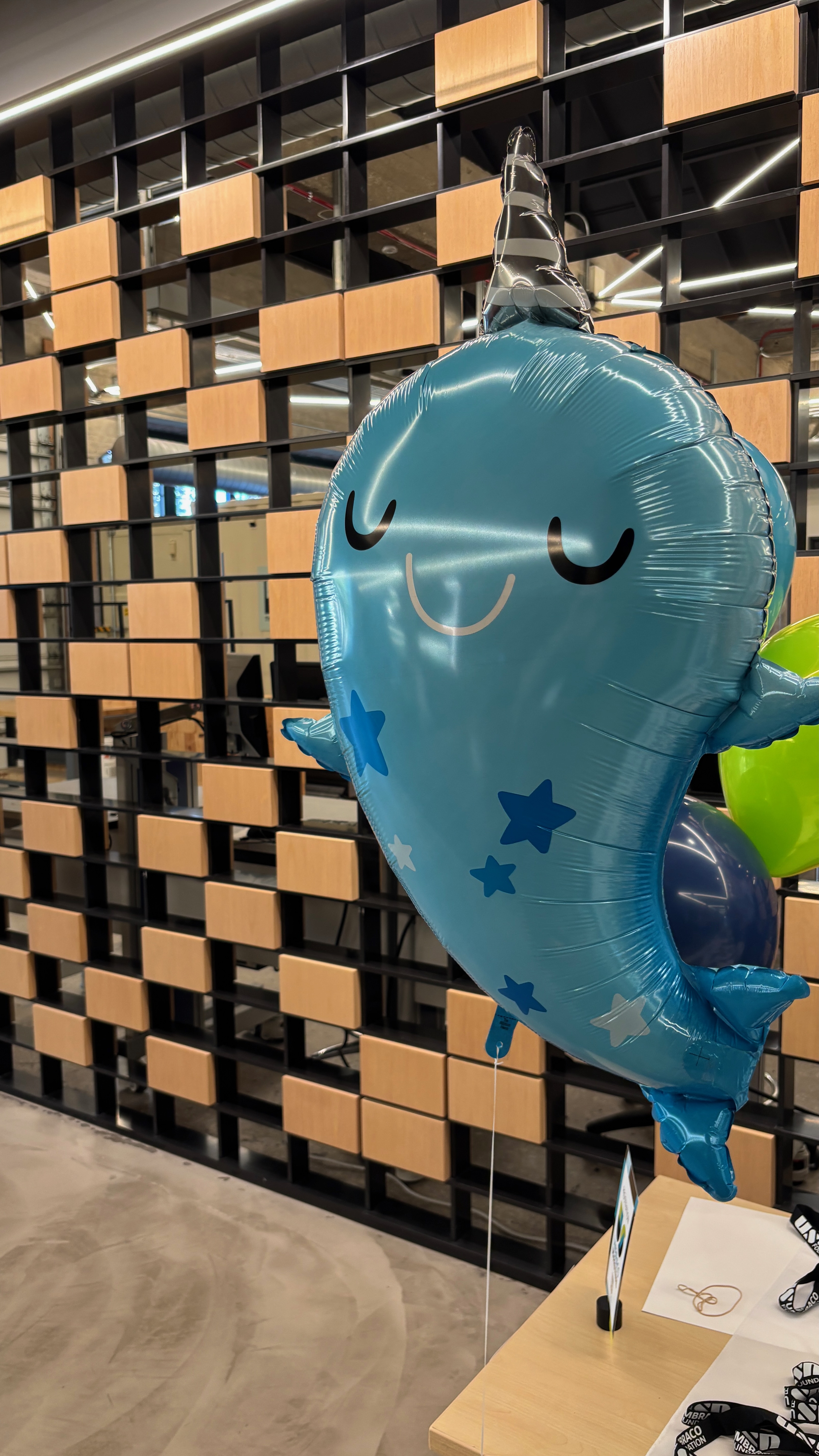 An image of a mylar balloon of a cartoon narwhal, smiling. In the background is a pattern of wooden blocks.