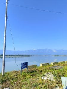 A picture of a Mahakali river, in Nepal with a blue board on the edge of a river written in Nepali language. The other side of the river has a green hills and clear blue sky.
