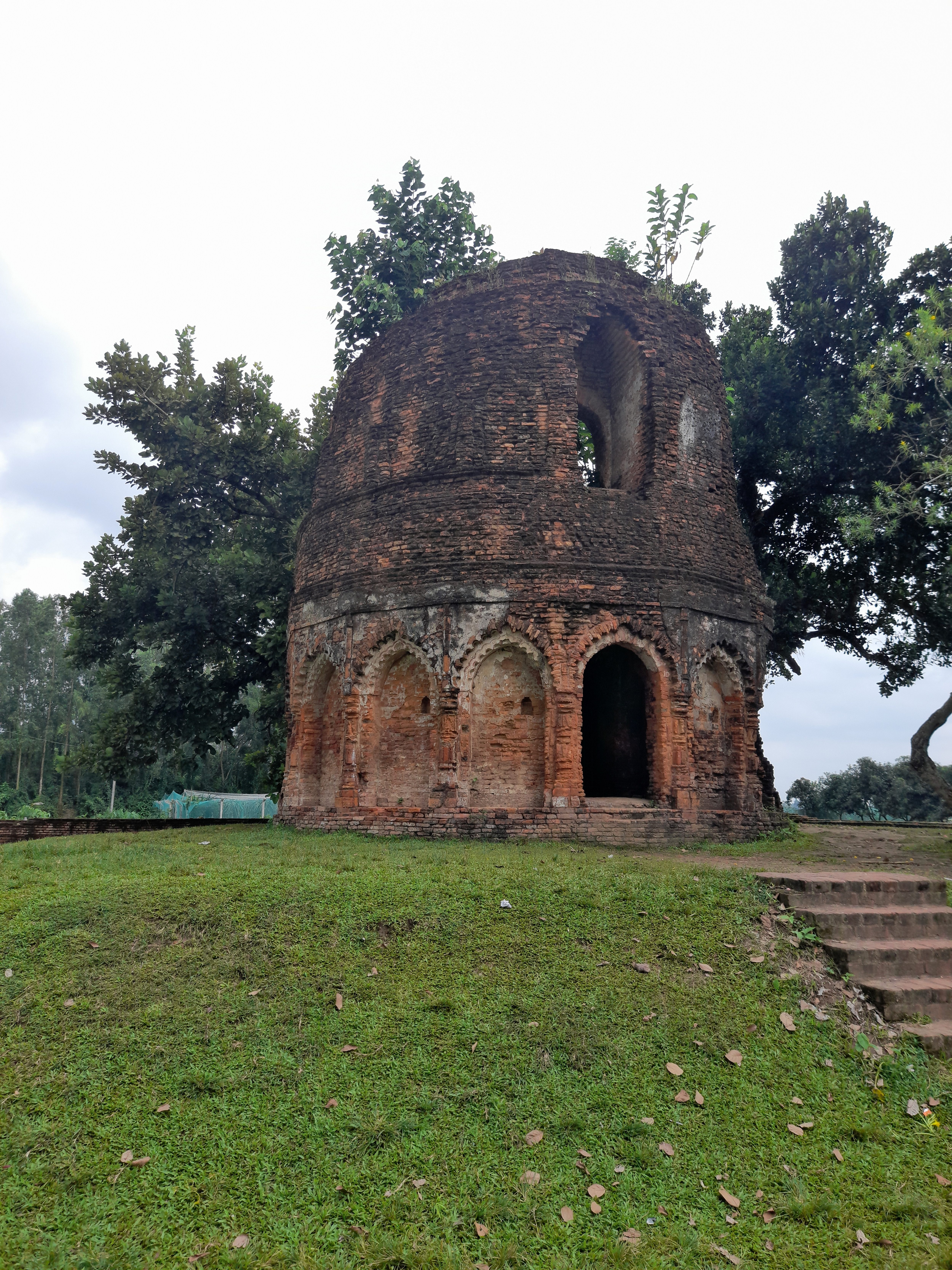 

Ancient red brick arches amid green grass and trees under a calm, cloudy sky.