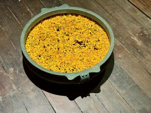 A traditional brass uruli filled with yellow marigold petals, placed on a wooden floor near Cherai Beach, Kerala.