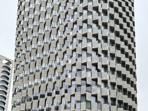 A modern building wall shows a 3D pattern. Square blocks stick out and go in, like a checkerboard, with windows in between.