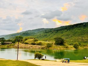 A dramatic scene at Niladri Lake, Sylhet, Bangladesh, Lush, dark green hills cascade down to the still, turquoise water, reflecting patches of brilliant golden sunset light that pierce through a cloudy sky