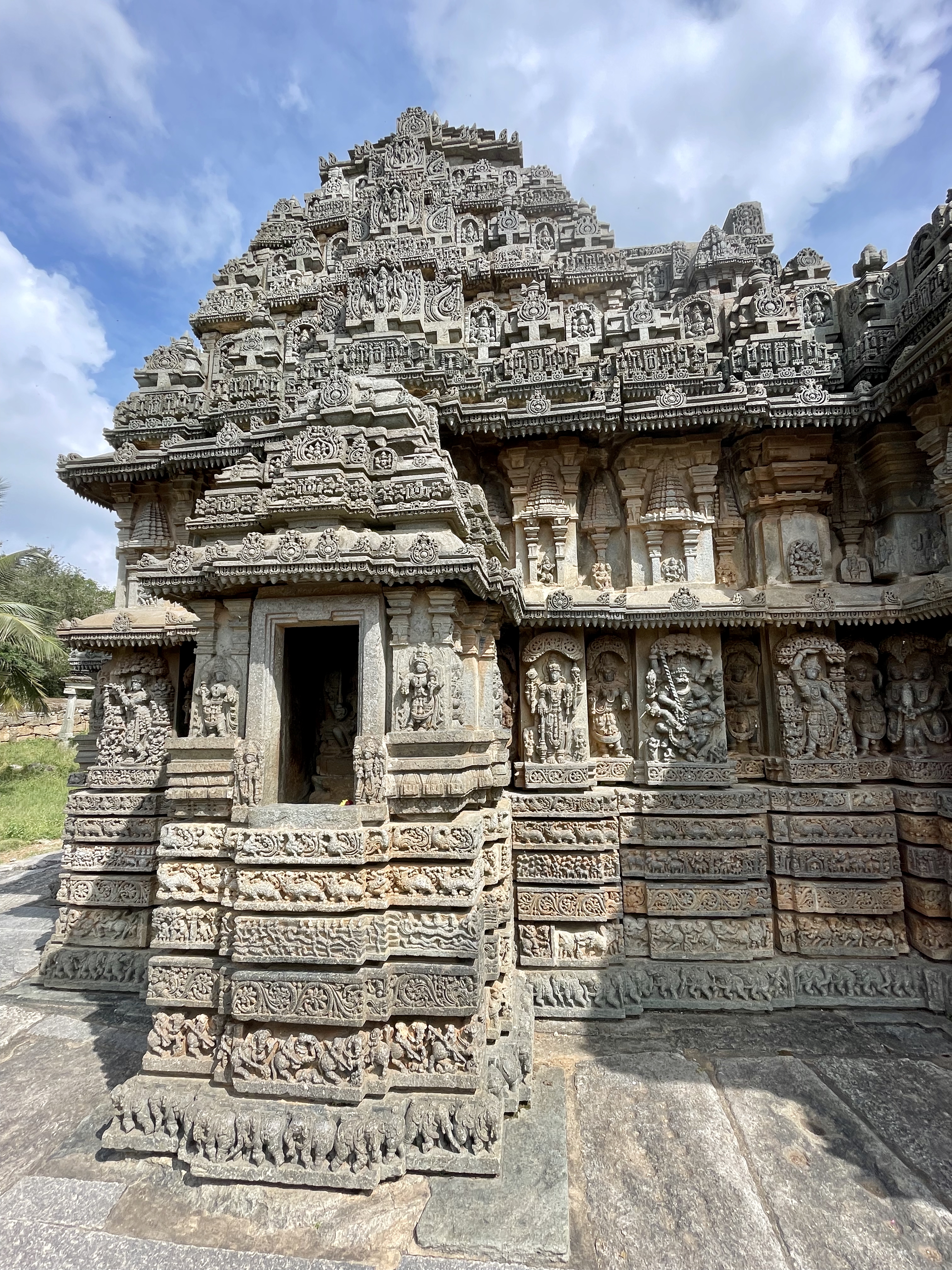 Intricate carvings cover the temple tower at the Lakshmi Narasimha Temple in Nuggehalli, Hassan. The image captures the layered structure and detailed sculptures under bright daylight. 