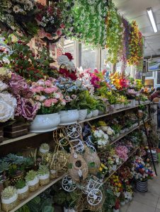 Artificial Flowers hung and kept on multiple flower pots for selling with a tubelight on the ceiling.