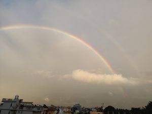 A vibrant rainbow arcs across a cloudy sky, with a faint double rainbow visible above it. 