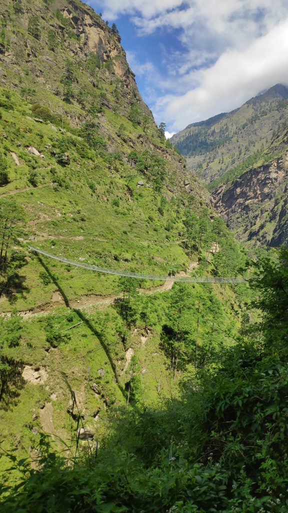 A lush green landscape featuring steep hills and rocky cliffs, with a blue sky and fluffy white clouds above.